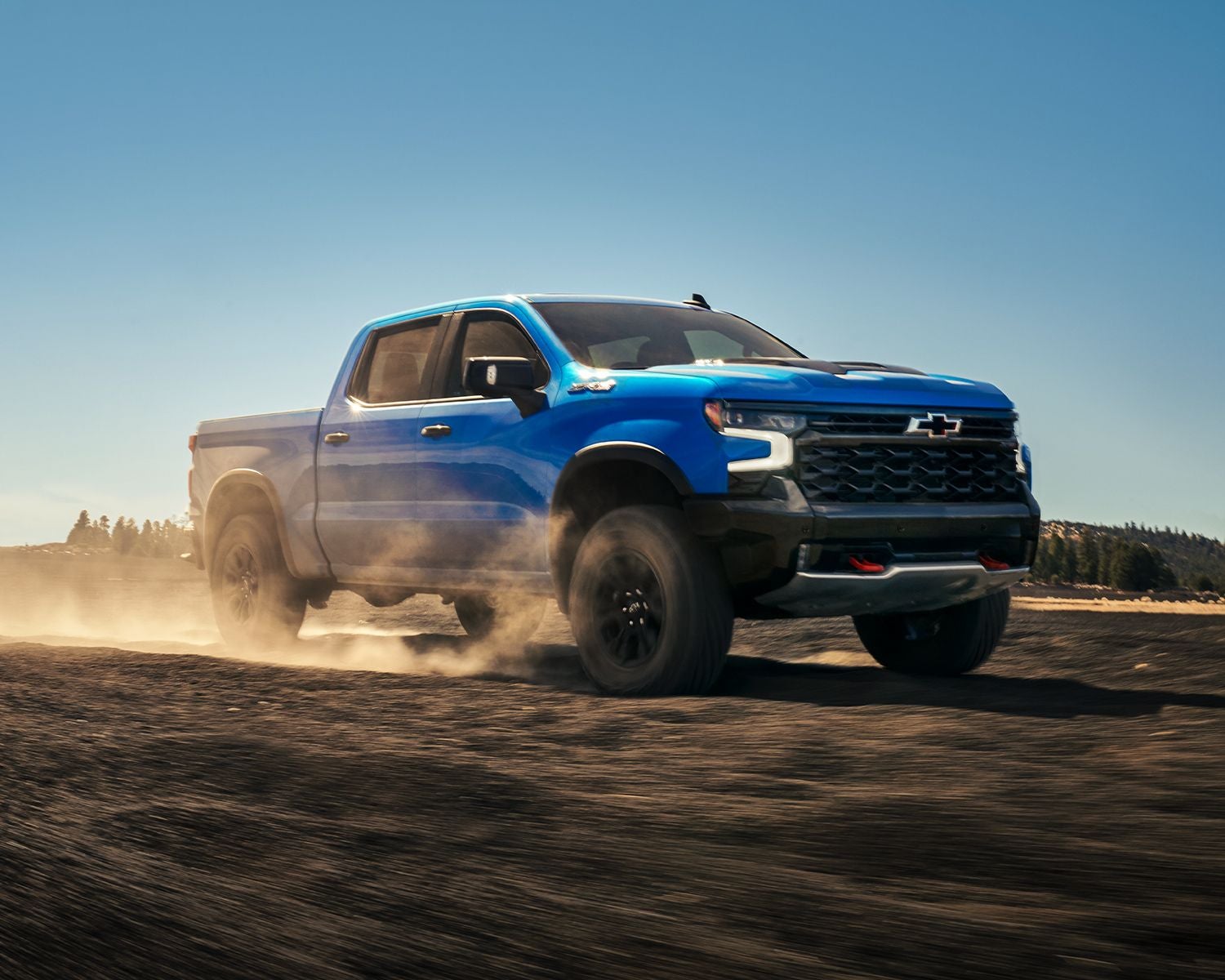 Front 3/4 shot of the 2025 Chevrolet Silverado 1500 driving offroad on dirt path kicking up dust.