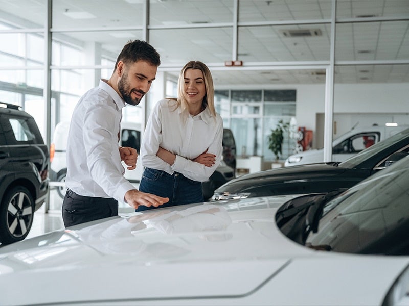 Two people in dress clothes looking at a vehicle.